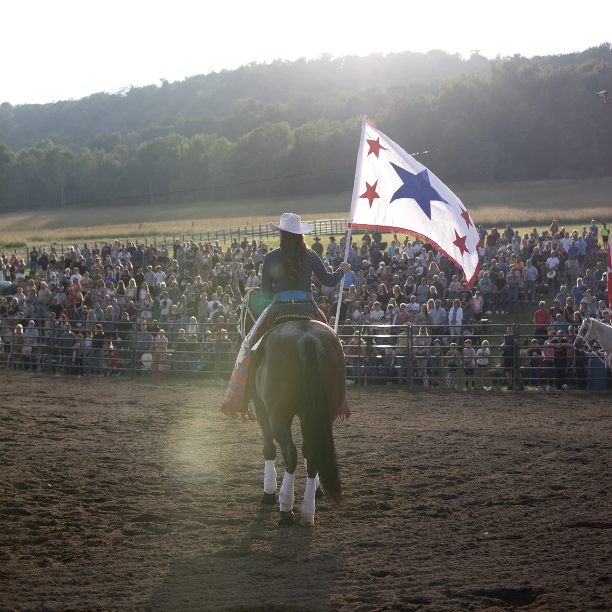 Woman holding a flag pole with right hand while riding a horse. Photo by Kaylin Kavanagh