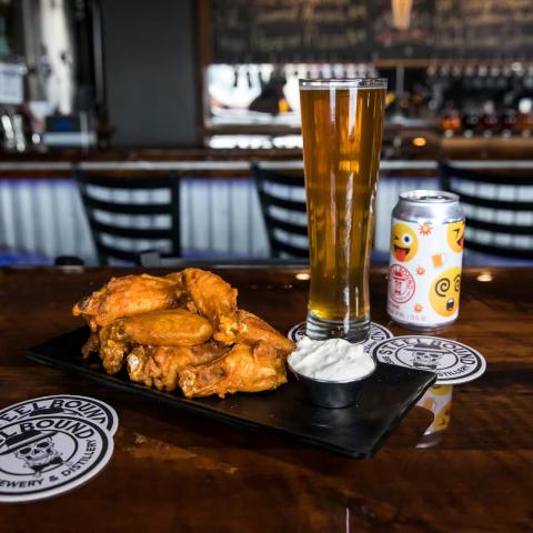 A plate of chicken wings, a glass of beer and a can of beer at Steelbound Brewery & Distillery